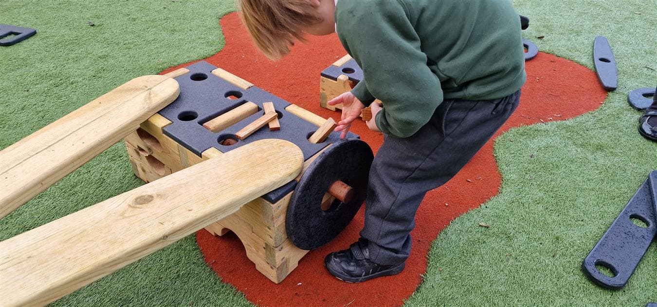 A young boy attaching a wheel to his role play playground equipment