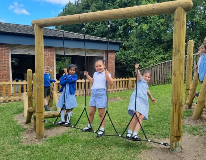 3 young girls climbing on the trim trail in the primary school playground 
