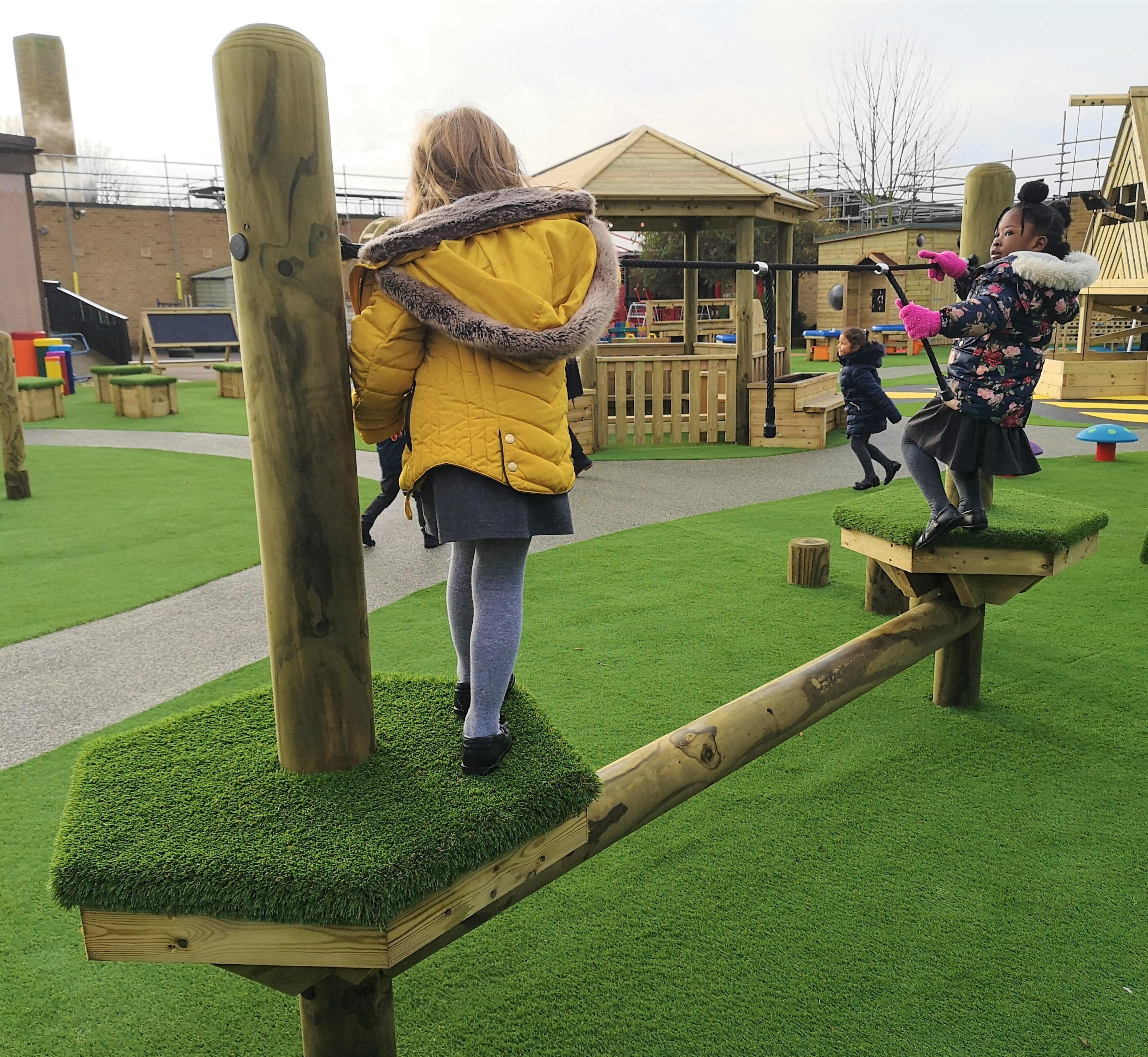 2 girls balancing on a trim trail in their playground