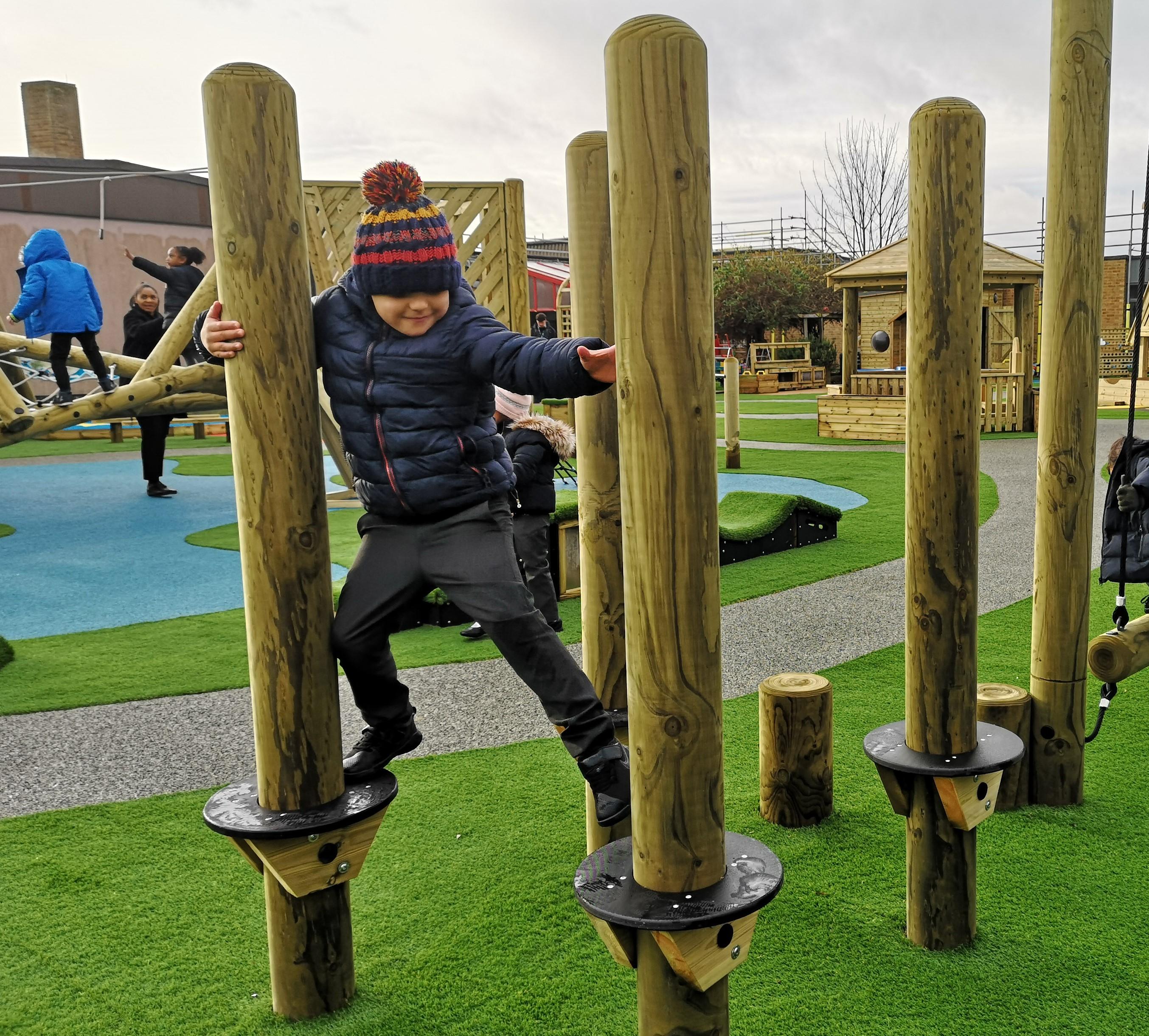 A young boy climbing across the trim trail in his primary school