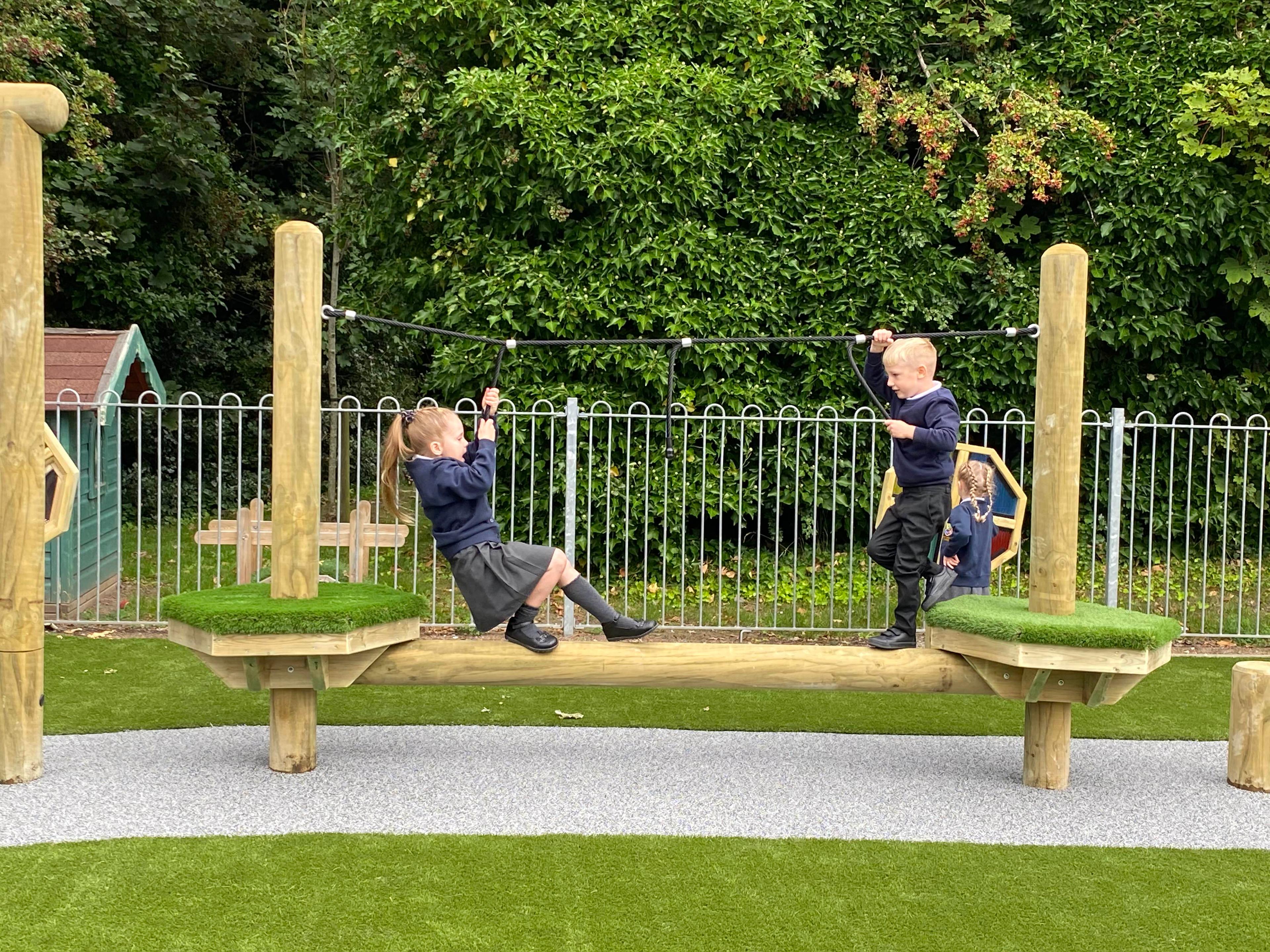2 children climbing across the trim trail in their playground