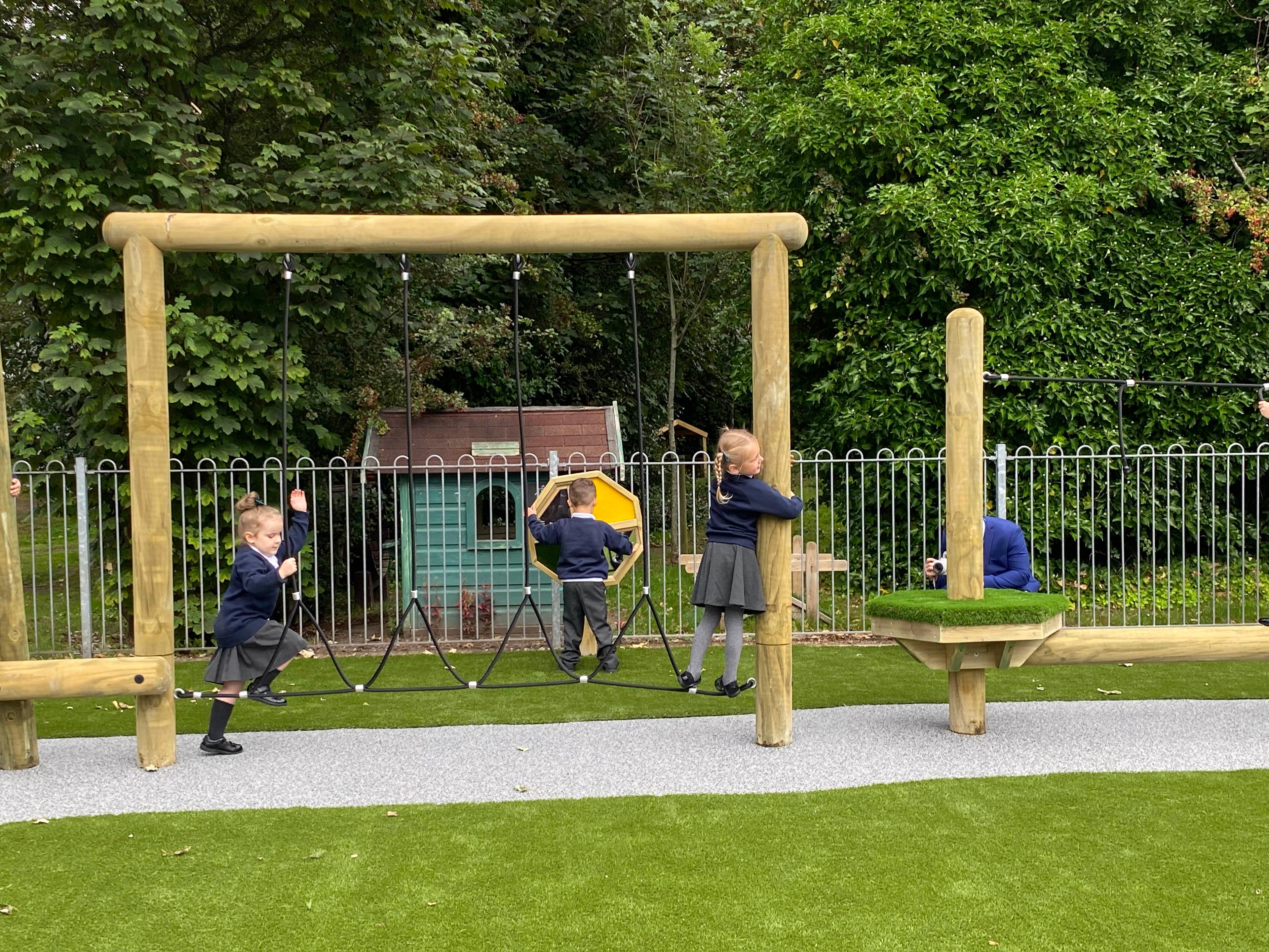 A class of children climbing across the balancing rope in their outdoor playground