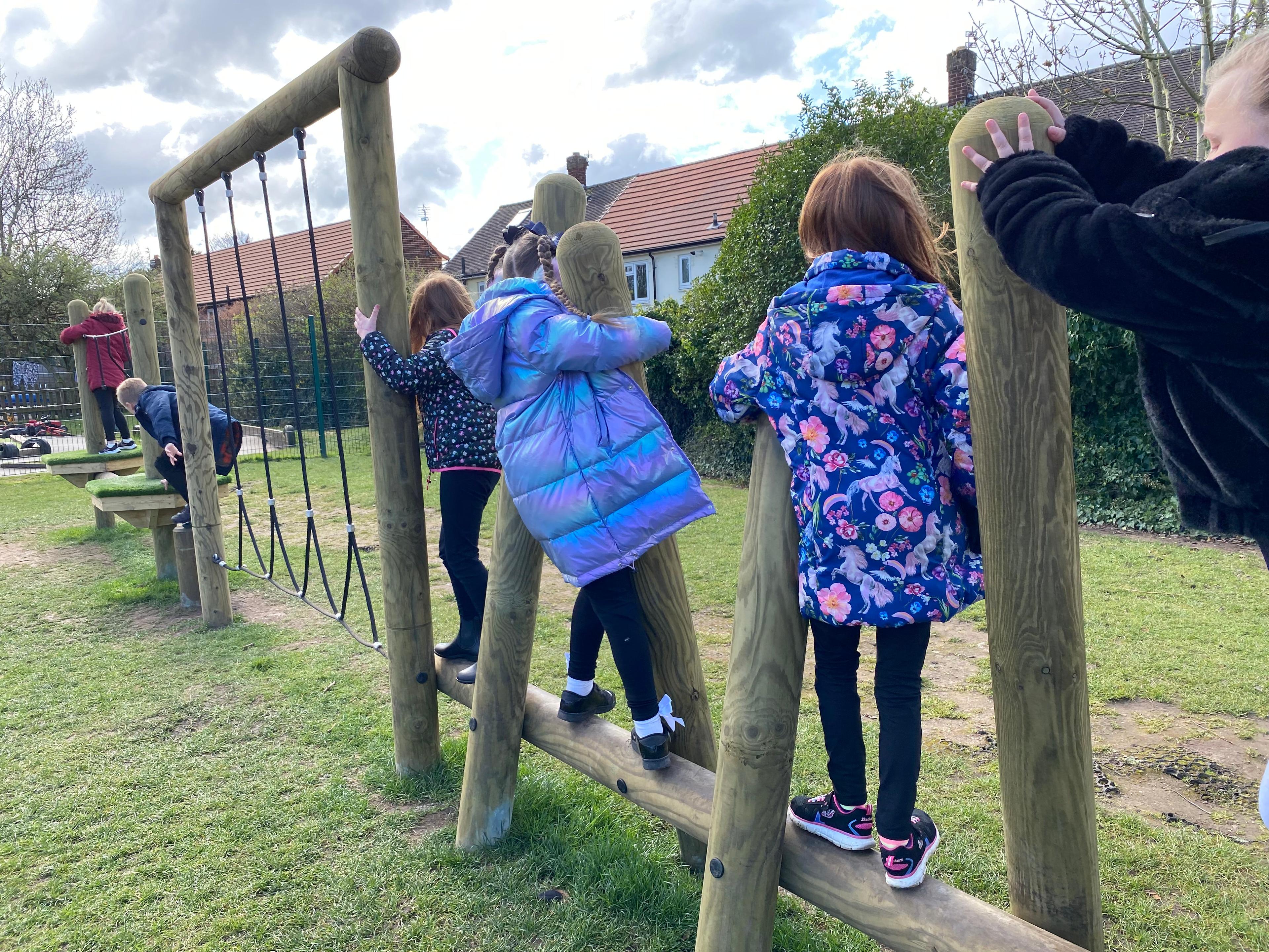 A class of children climbing up the balance beam in their playground