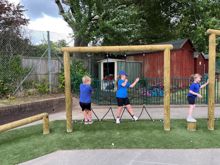 3 children waiting in turn to climb across the trim trail