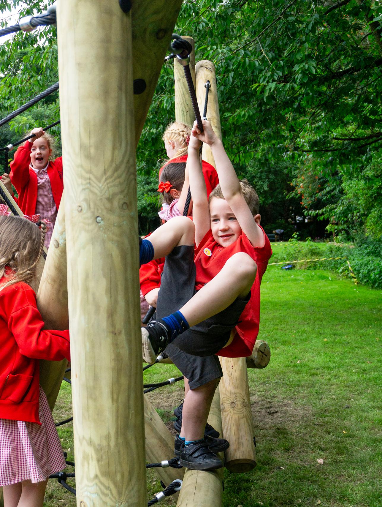 A boy is hanging off the ropes as he balances against a wooden pole.