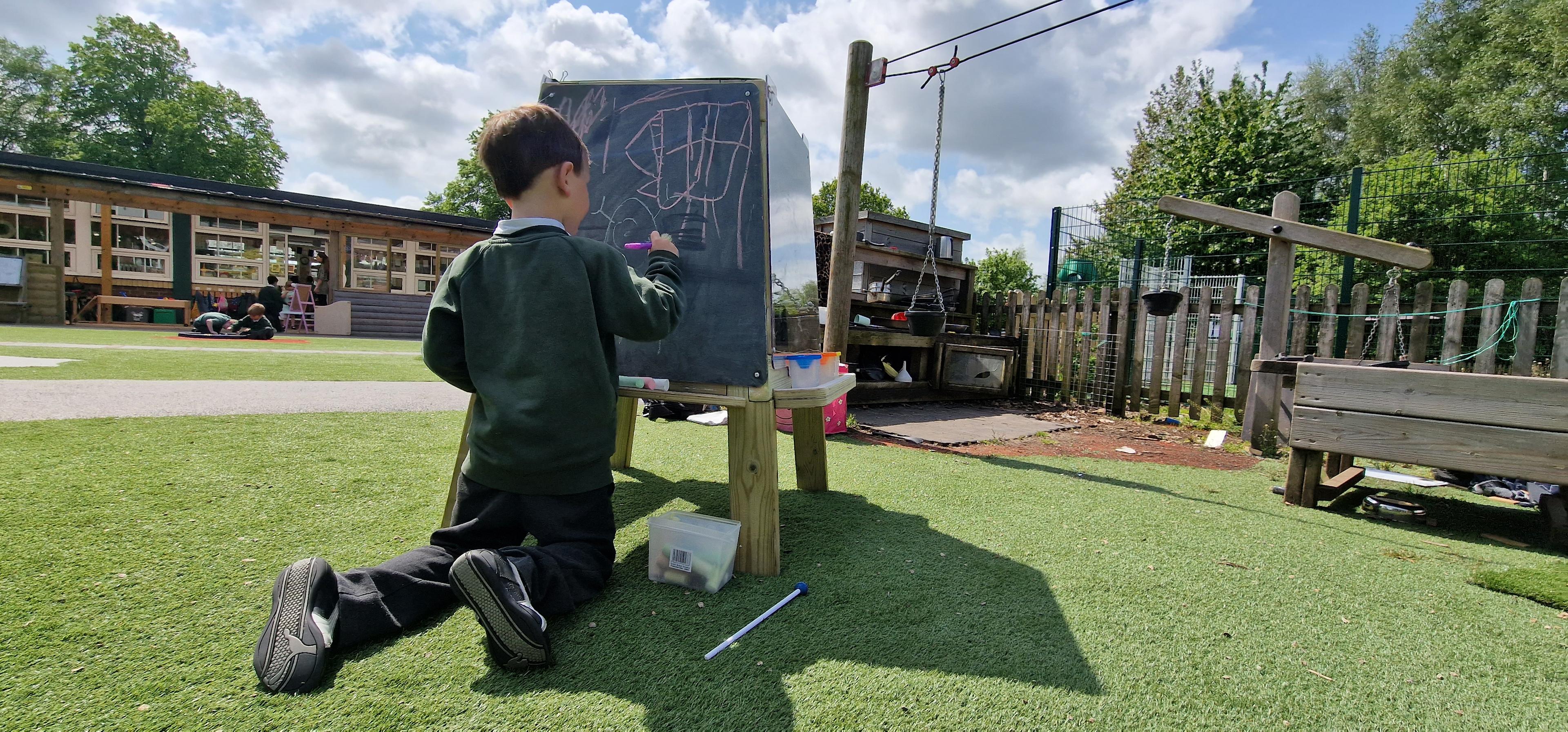 A child kneeling down on the floor next to the group art easel in his playground