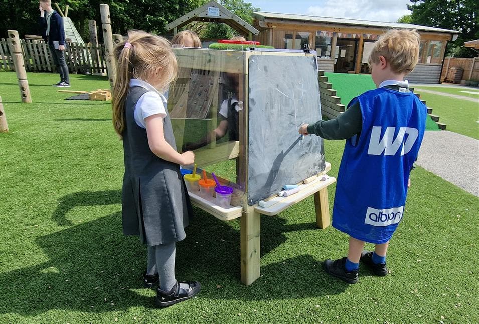 2 children drawing and painting on the group art easel in their playground 