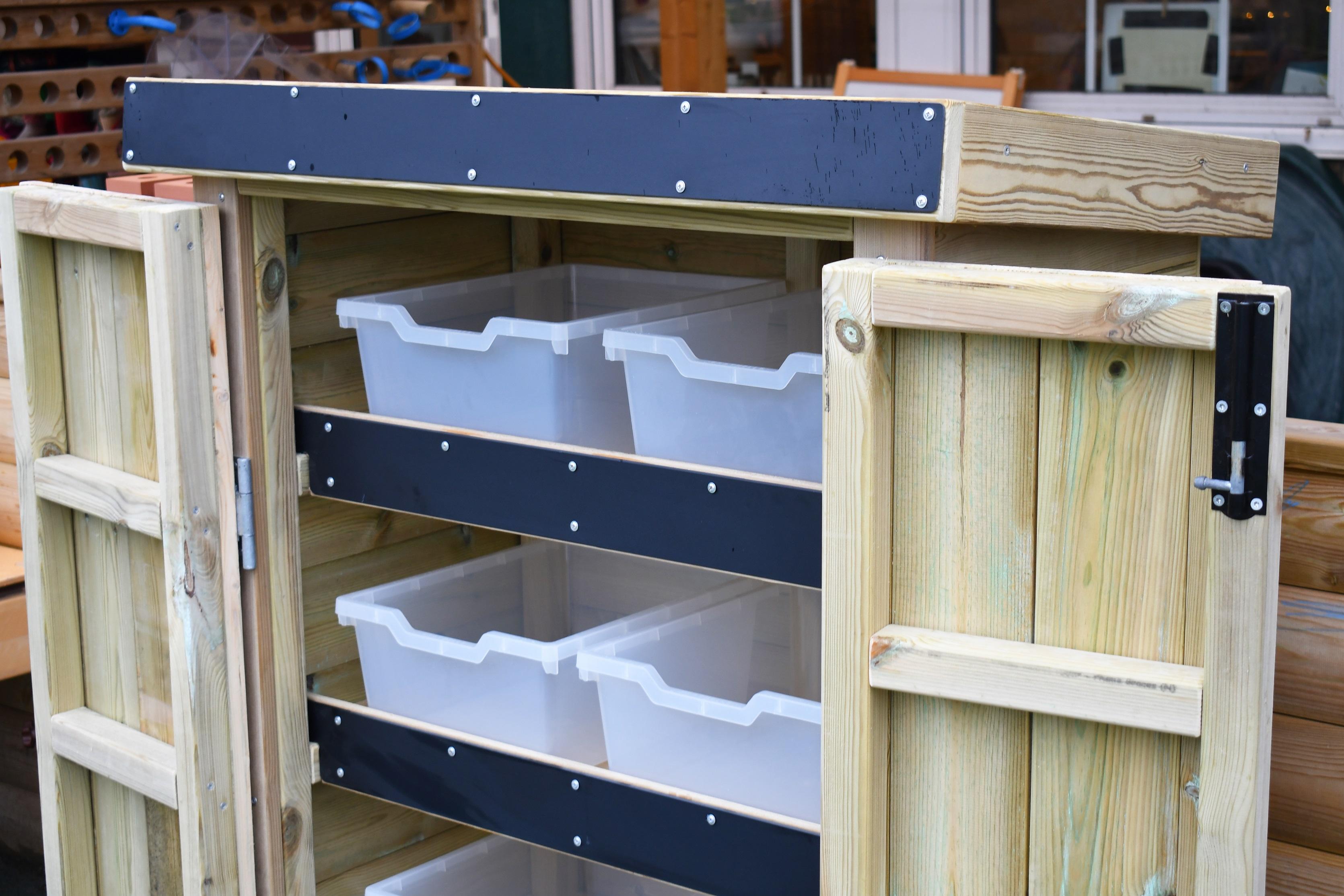 An open wooden Acorn Storage Unit with empty storage boxes inside, in a school playground