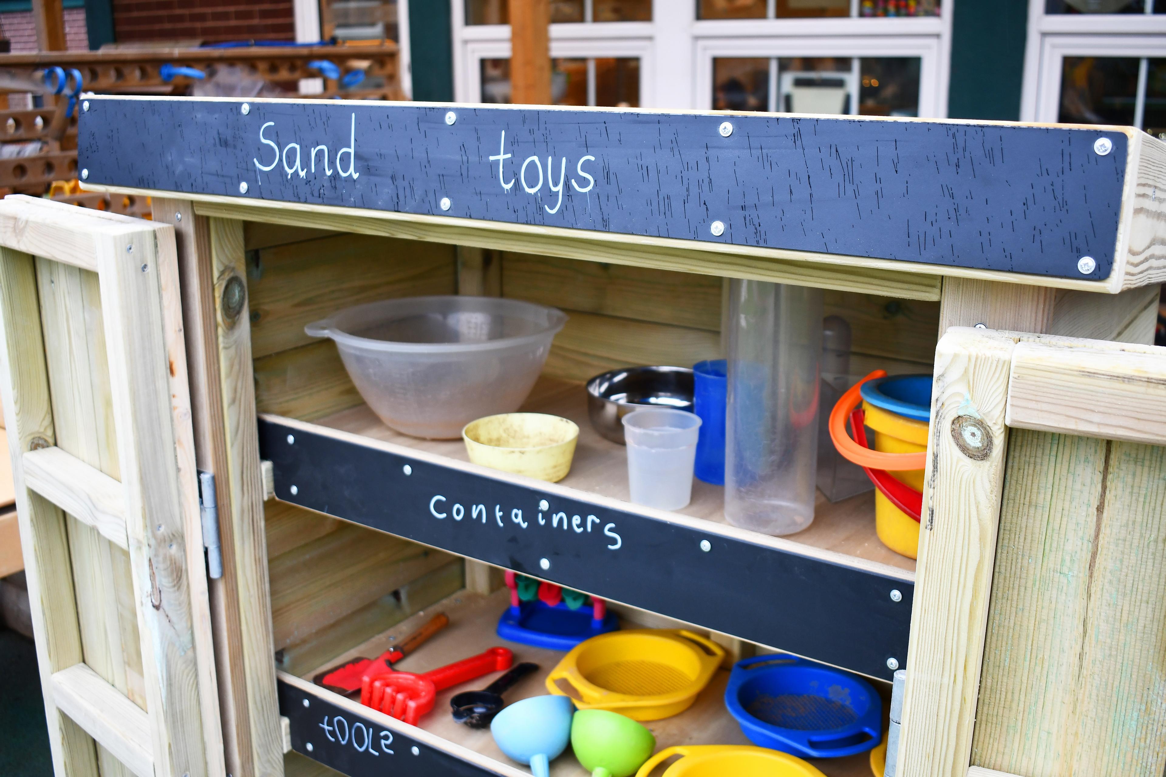 An open wooden Acorn Storage Unit with school resources inside, in a school playground