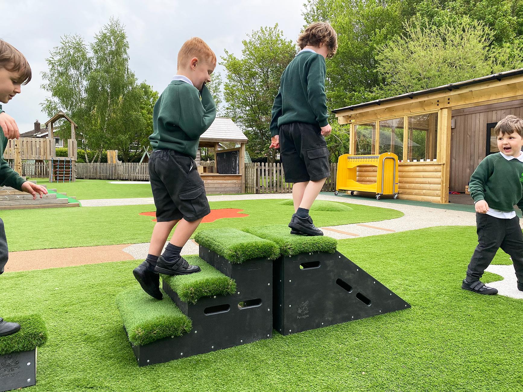 2 children wearing Kelsall Primary school uniform are playing with the Get Set, Go! Blocks. One child is climbing the step block whilst the other is stood on top of the slide block.