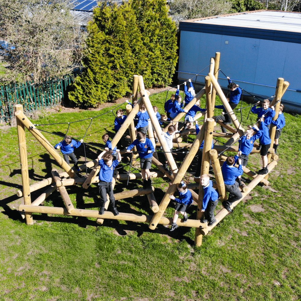 An overhead shout of a group of school children in blue jumpers playing on a large wooden climbing frame in a playground.