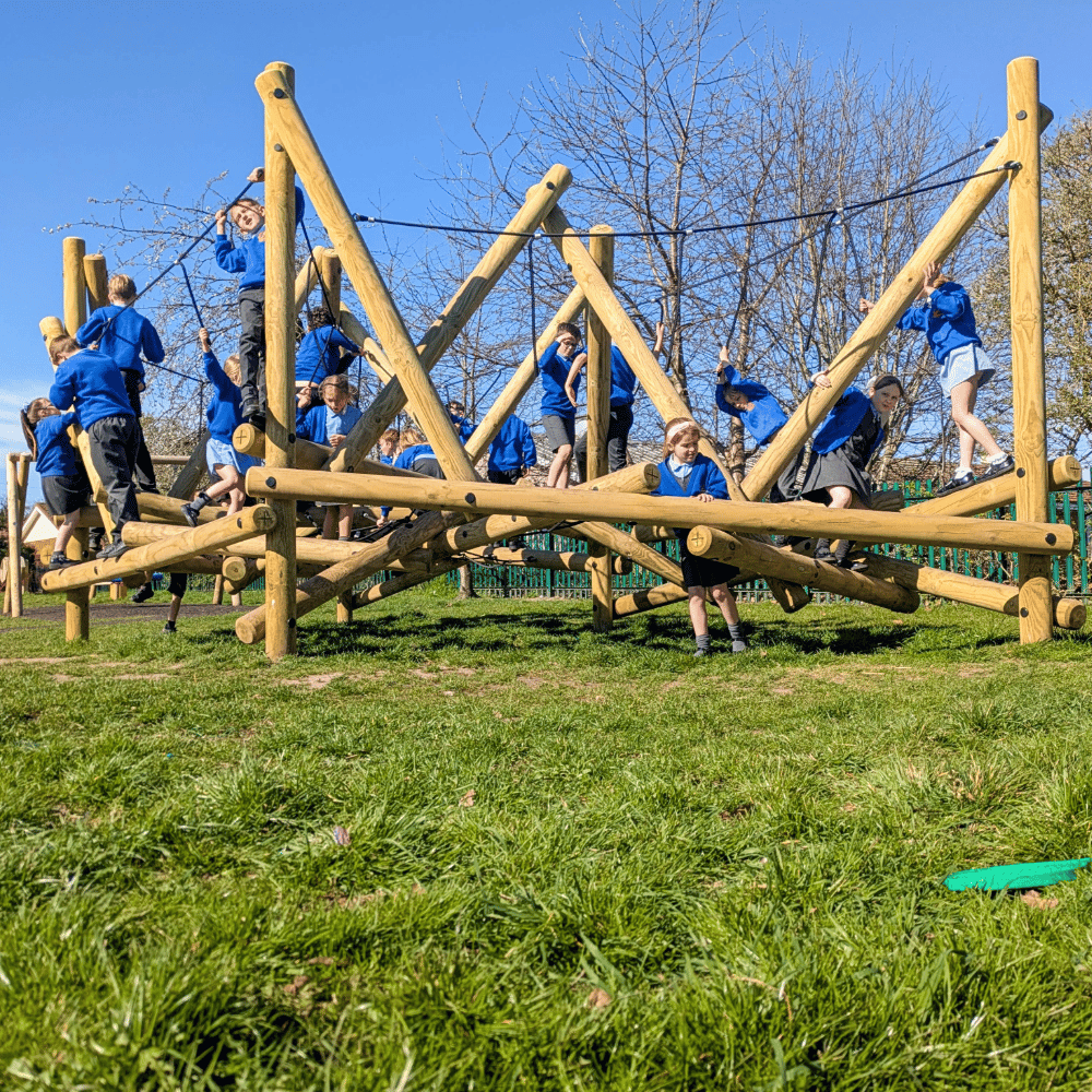 An low level shout of a group of school children in blue jumpers playing on a large wooden climbing frame in a playground.