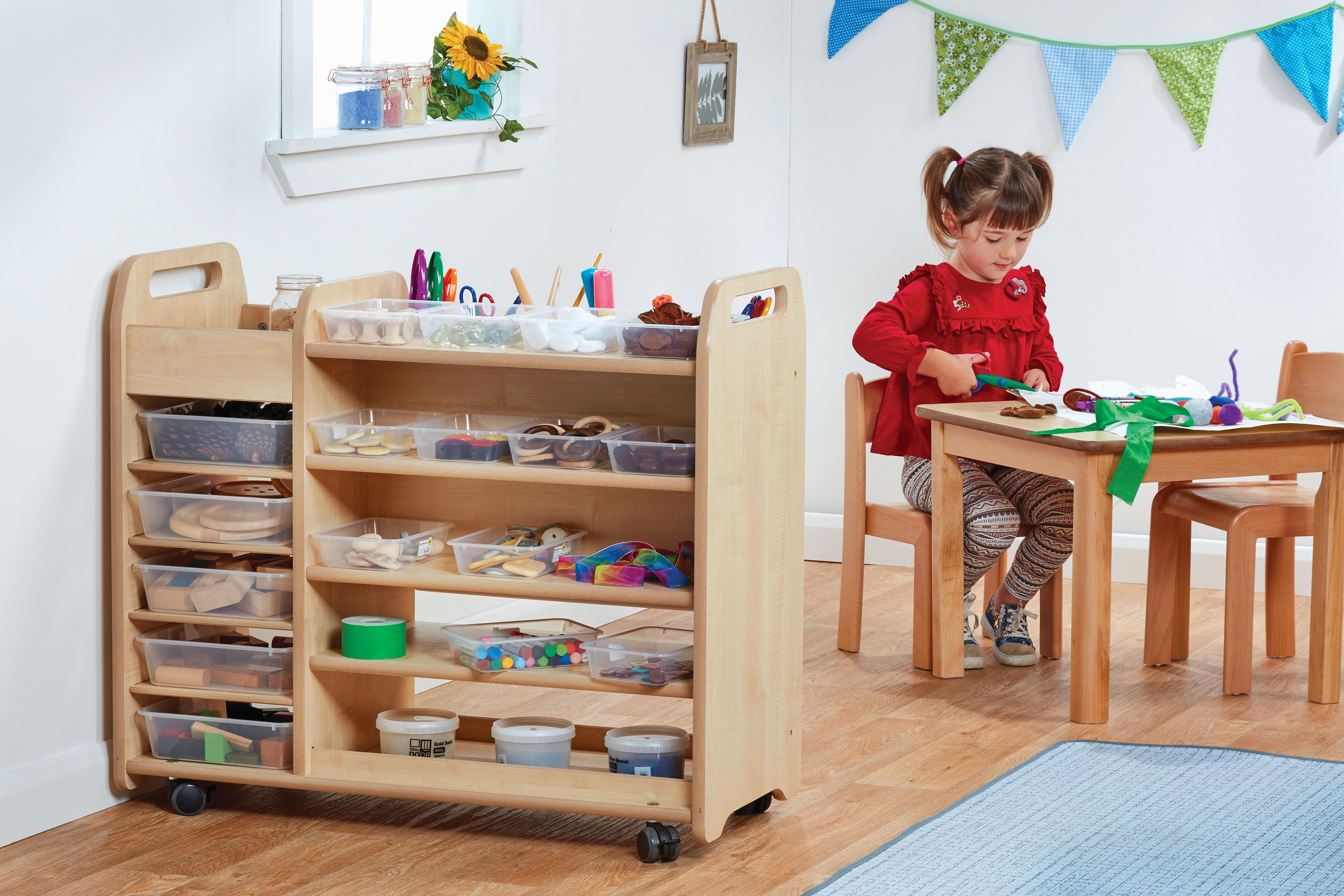 A young girl sitting in front of a Continuous Provision Trolley which is full of arts and crafts supplies