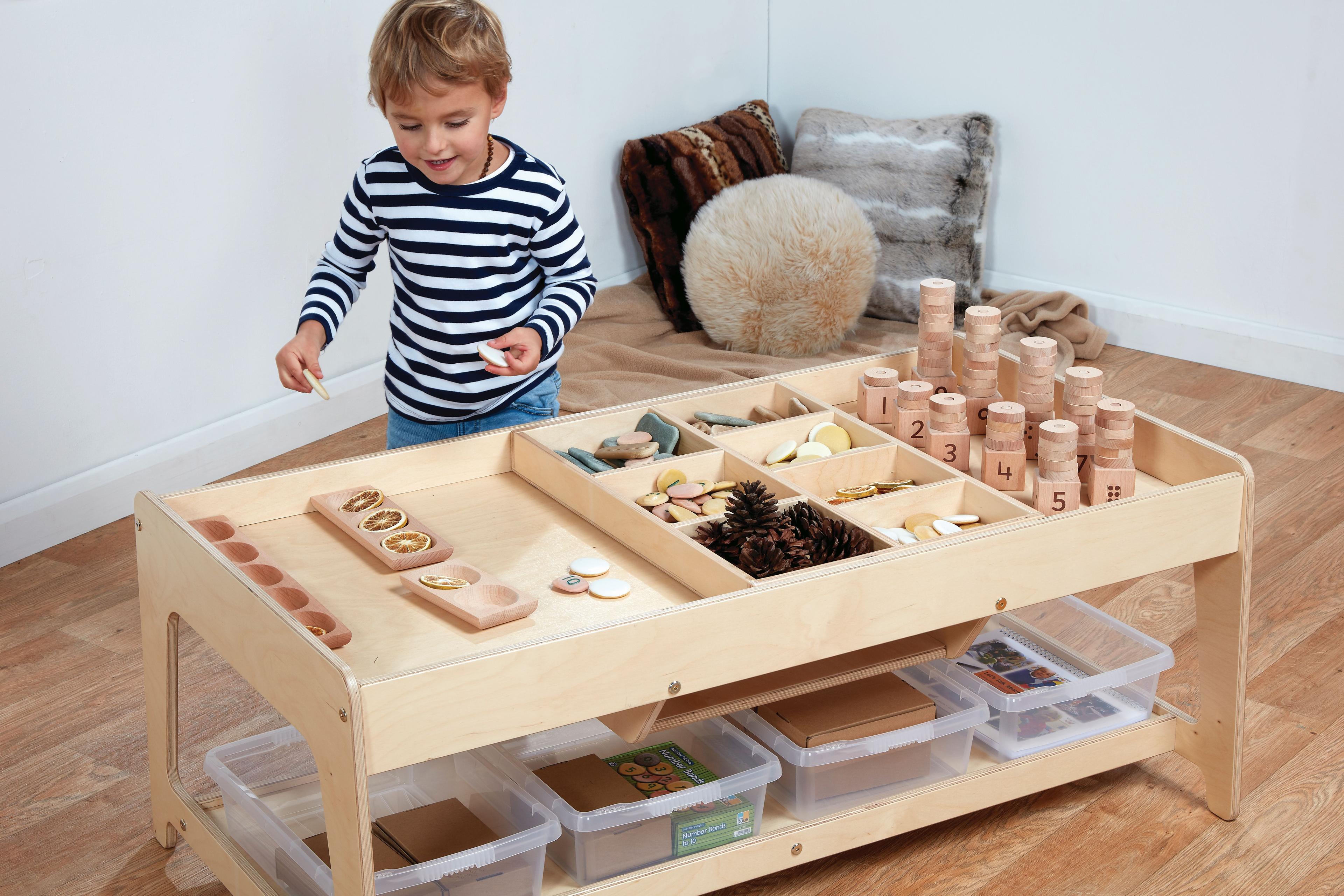 A toddler standing in front of the Investigative Play Table looking happy