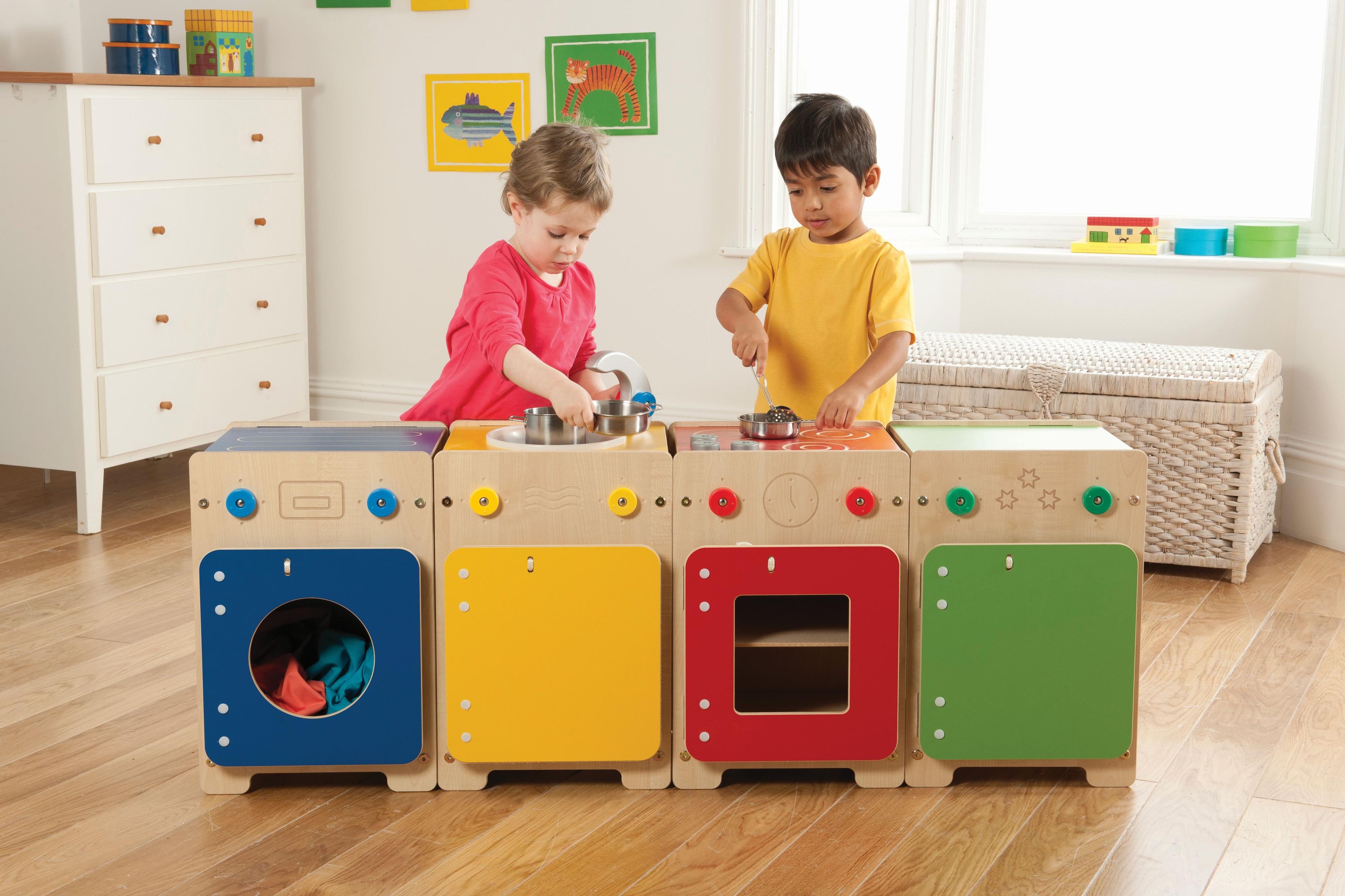 A young boy and girl are playing with the Wolds Kitchen Set (Sink, Washer, Cooker & Fridge), inside a classroom.