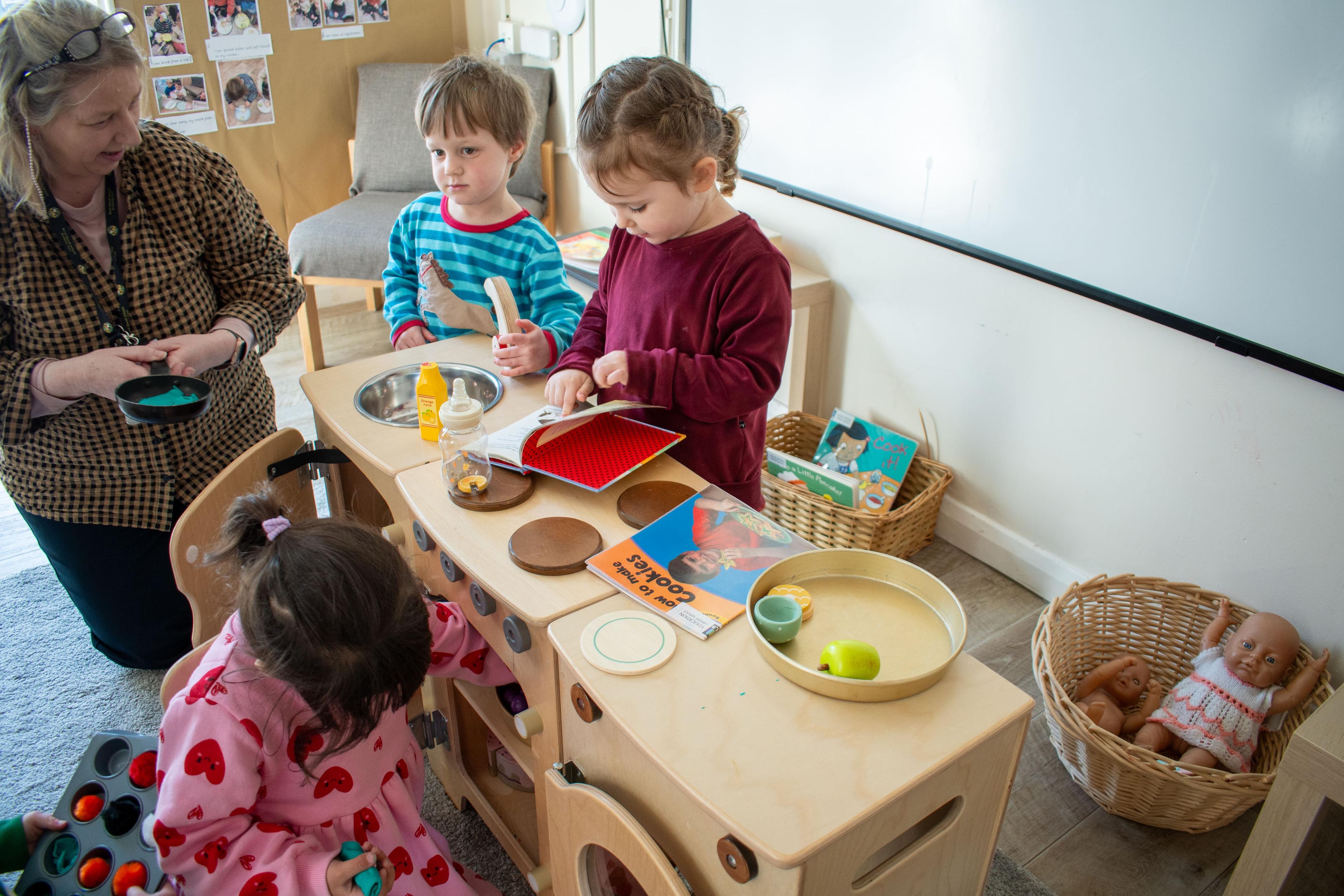 Nursery practitioner helping children use their Natural Kitchen set