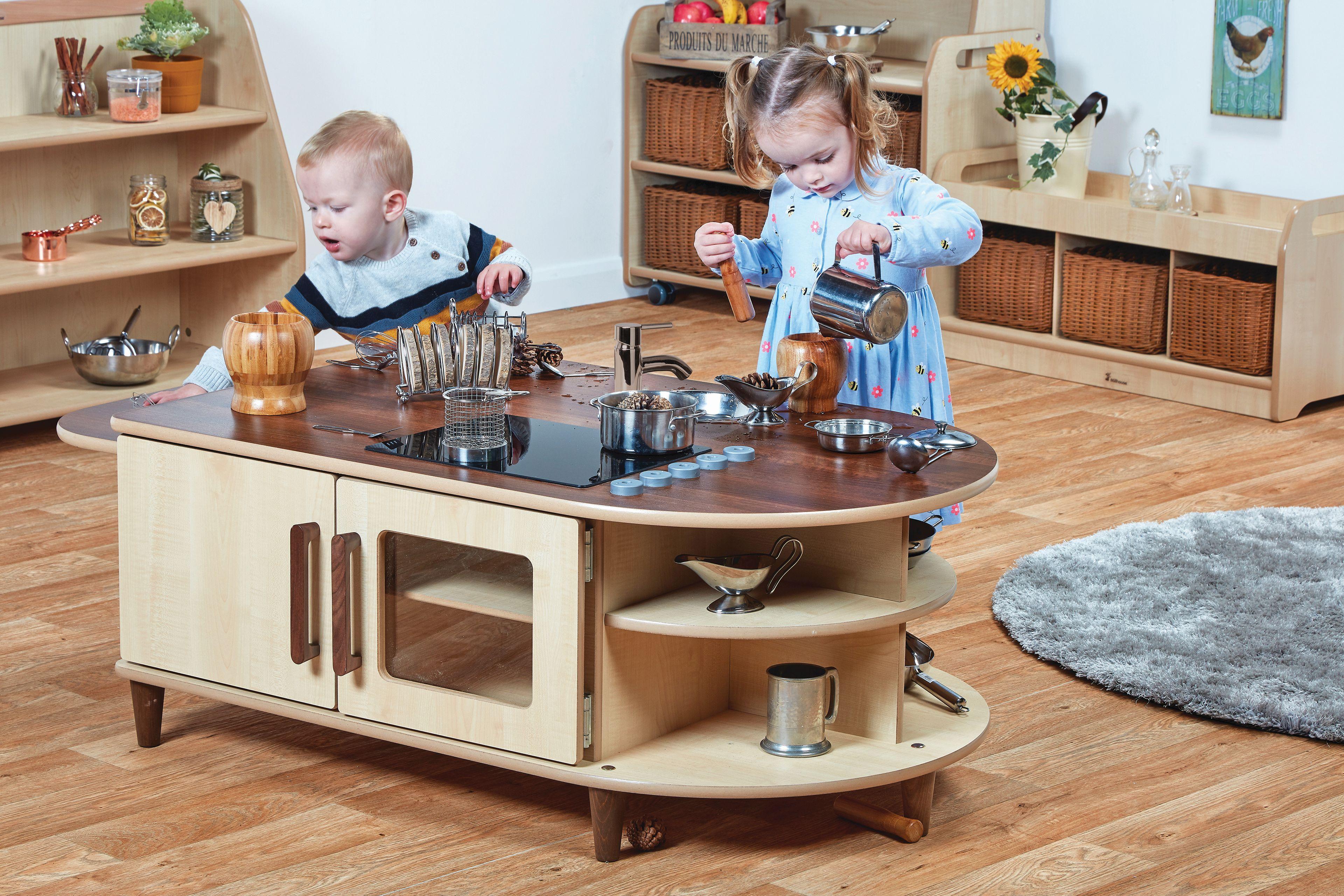 A wooden play-kitchen island with two toddlers playing on it in a nursery setting.