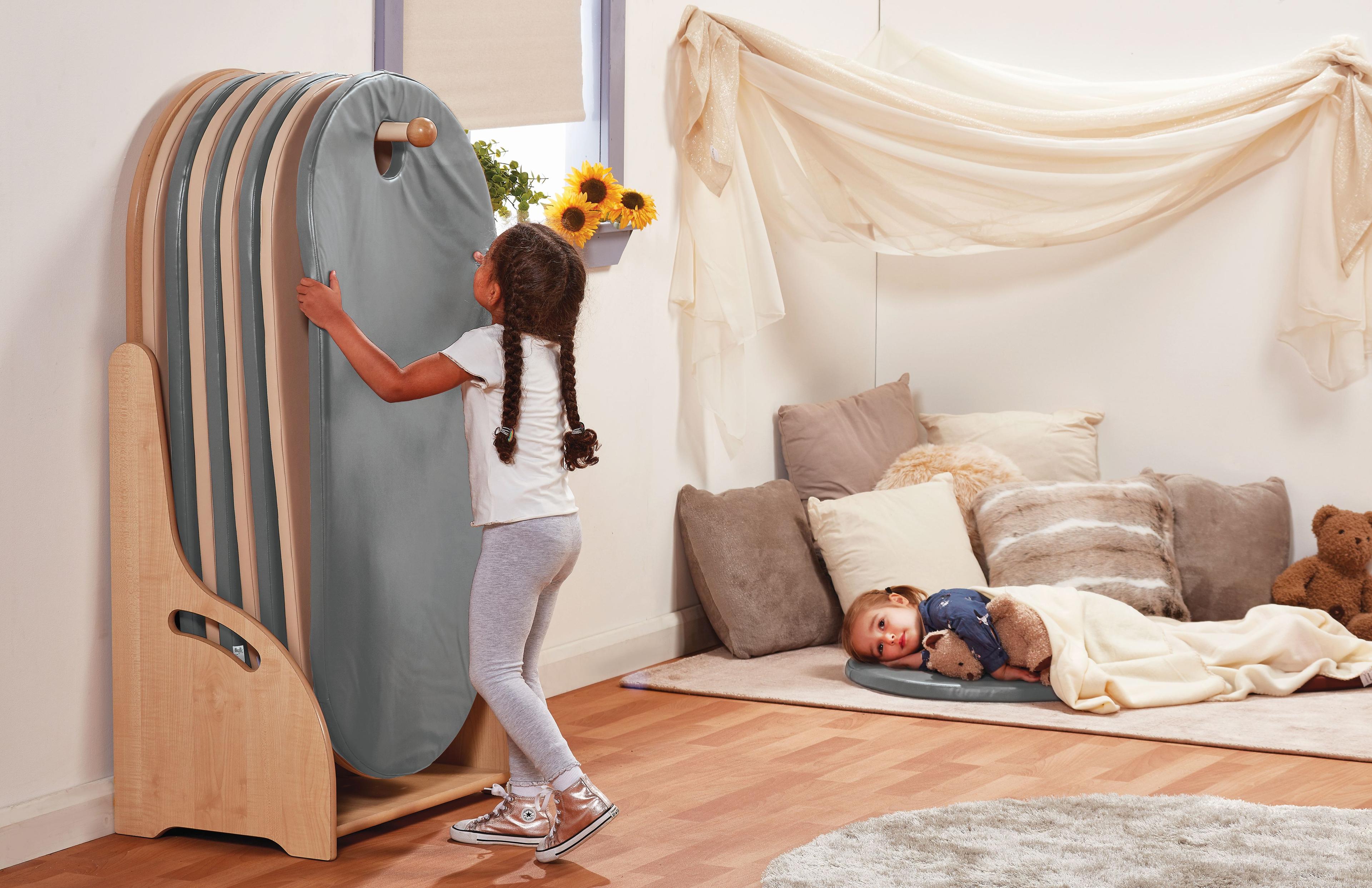 A young girl is lifting a grey sleeping mat from the freestanding Slumberstore, another girl is lying on a sleeping mat in the background.