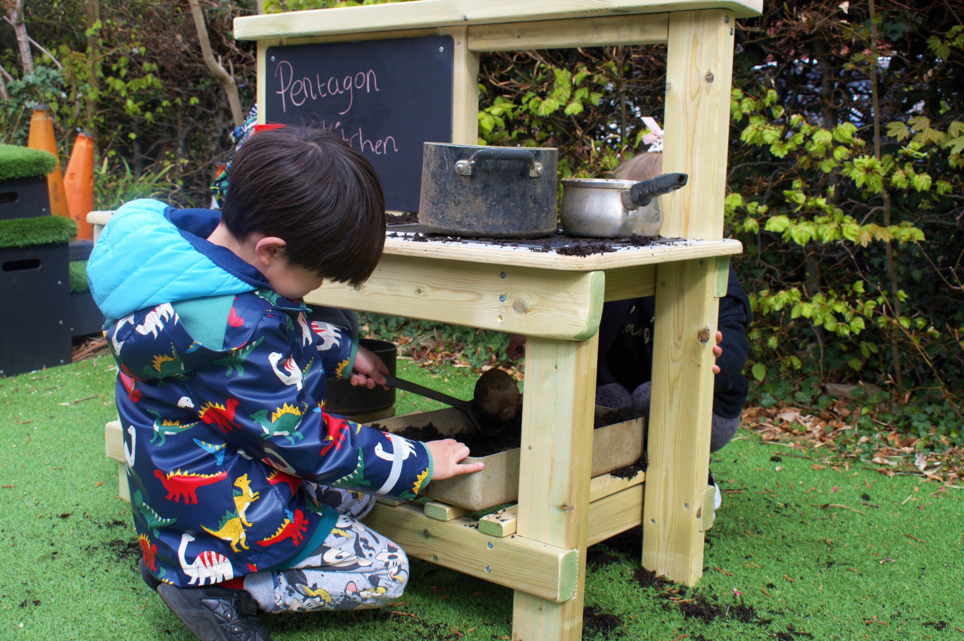 Little boy making mud recipes on a wooden mud kitchen