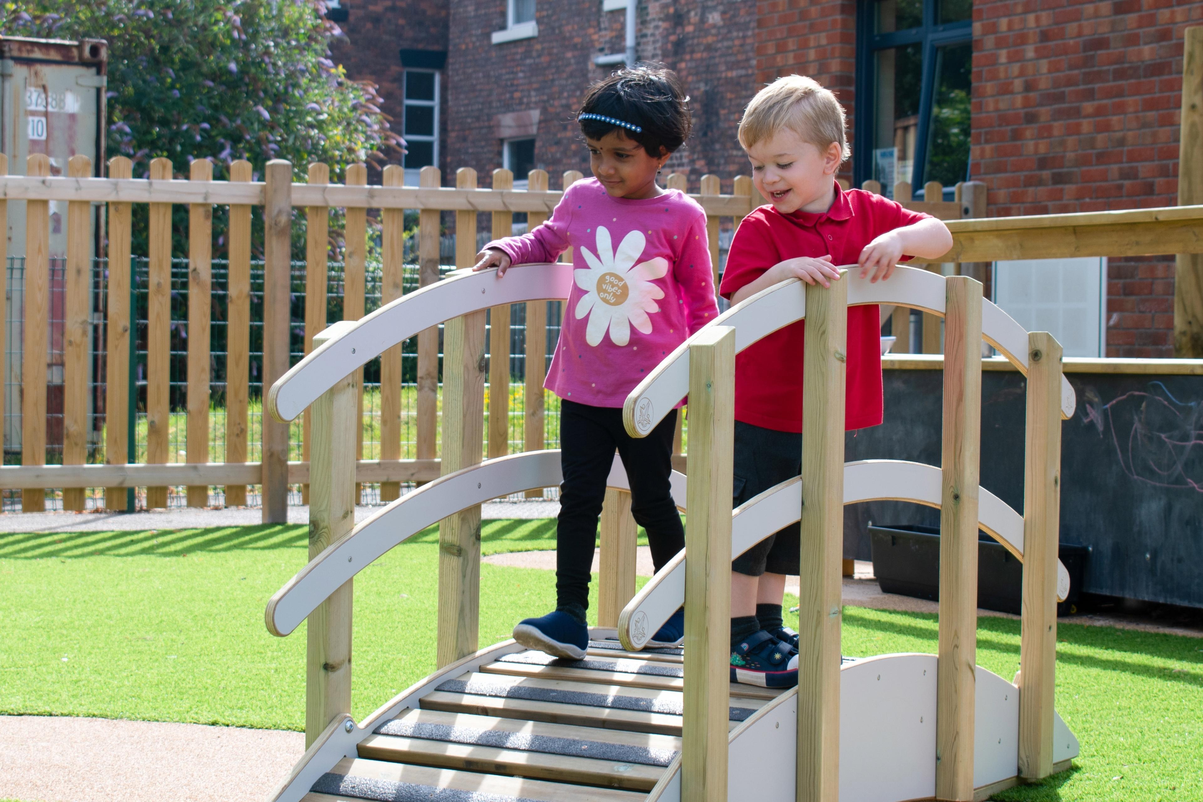 Two children walking across a play bridge holding onto the rails