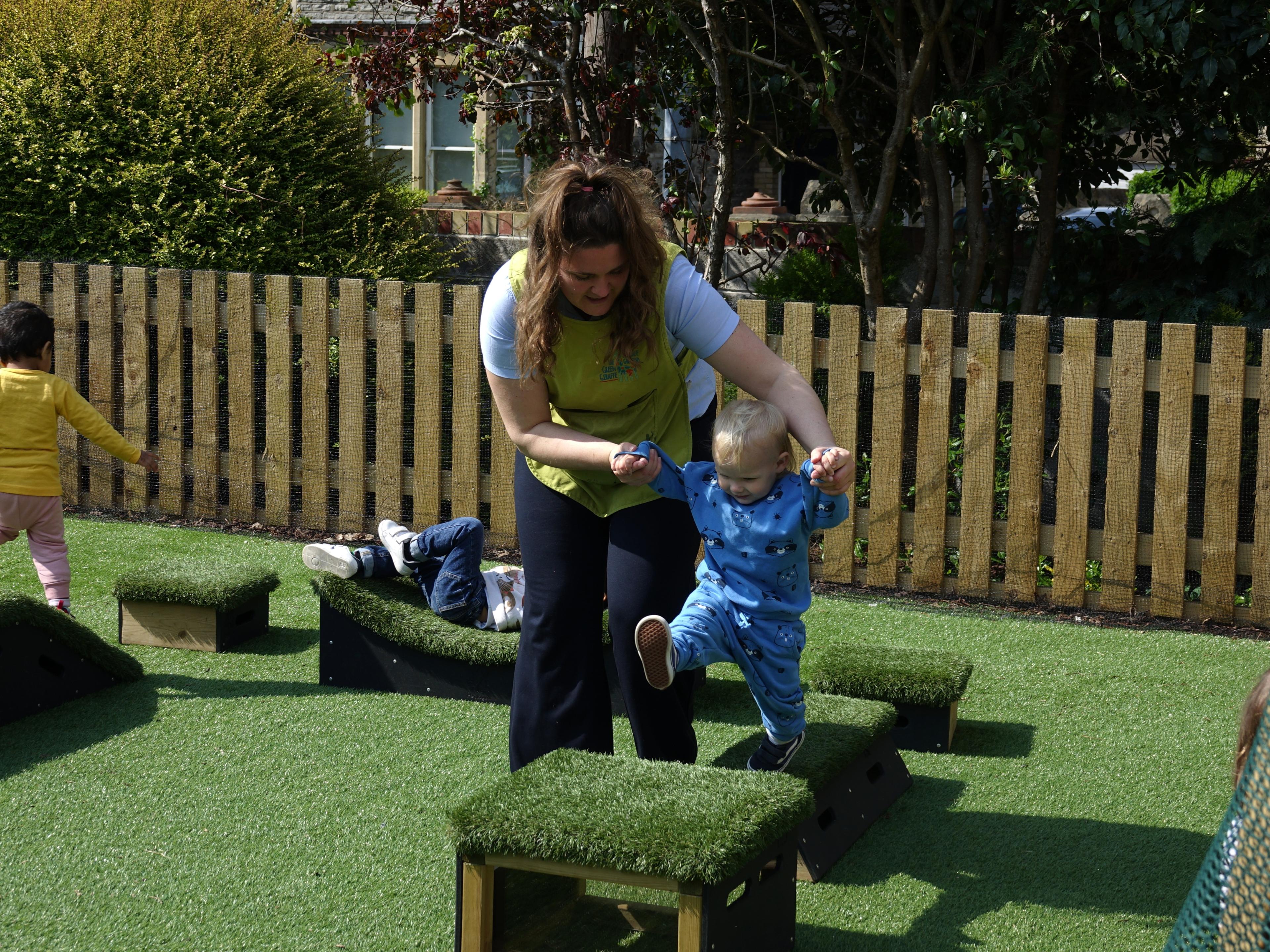 Baby being assisted to walk up a grass topped block