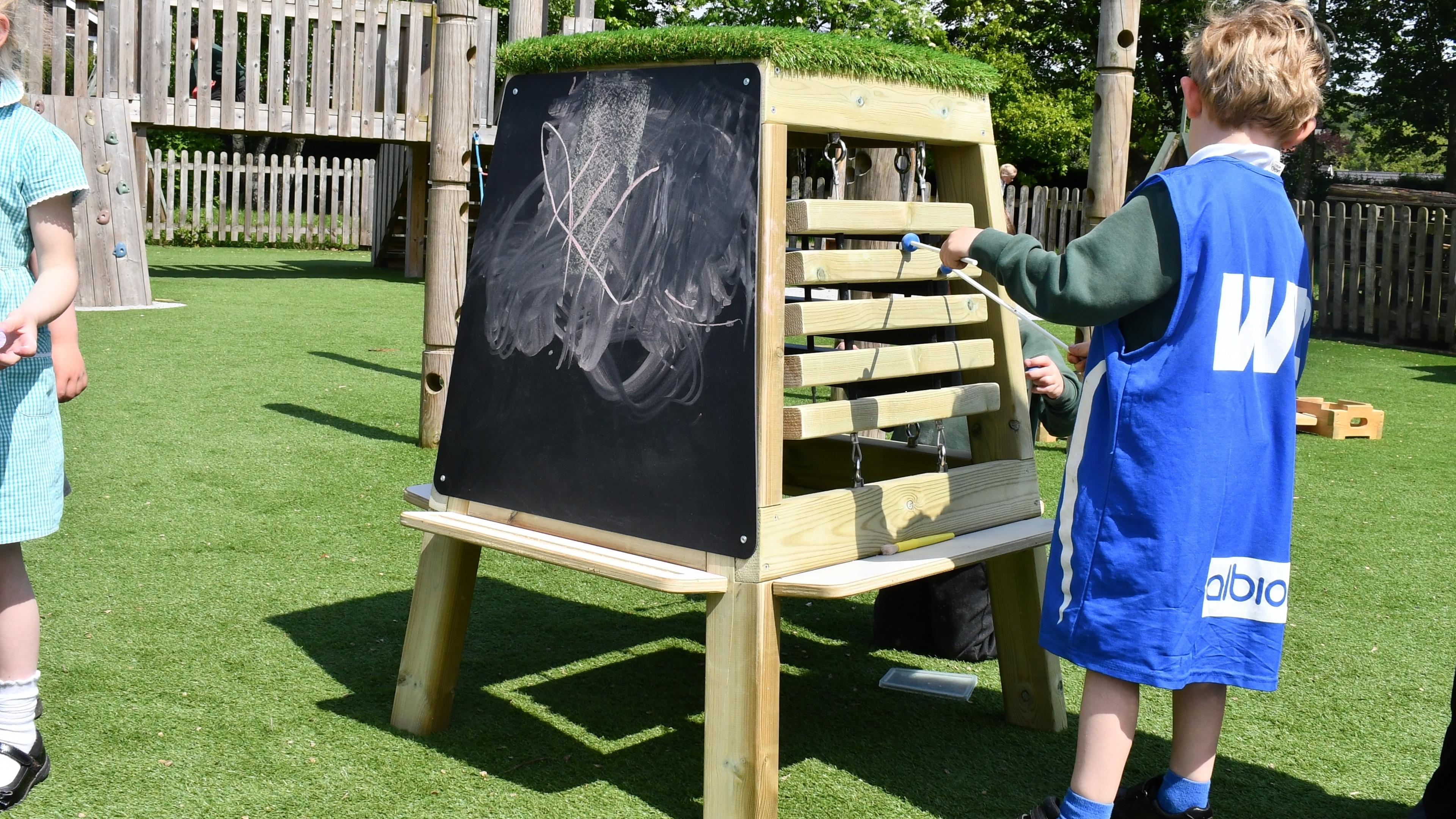 A boy playing music with a beater on a timber music easel