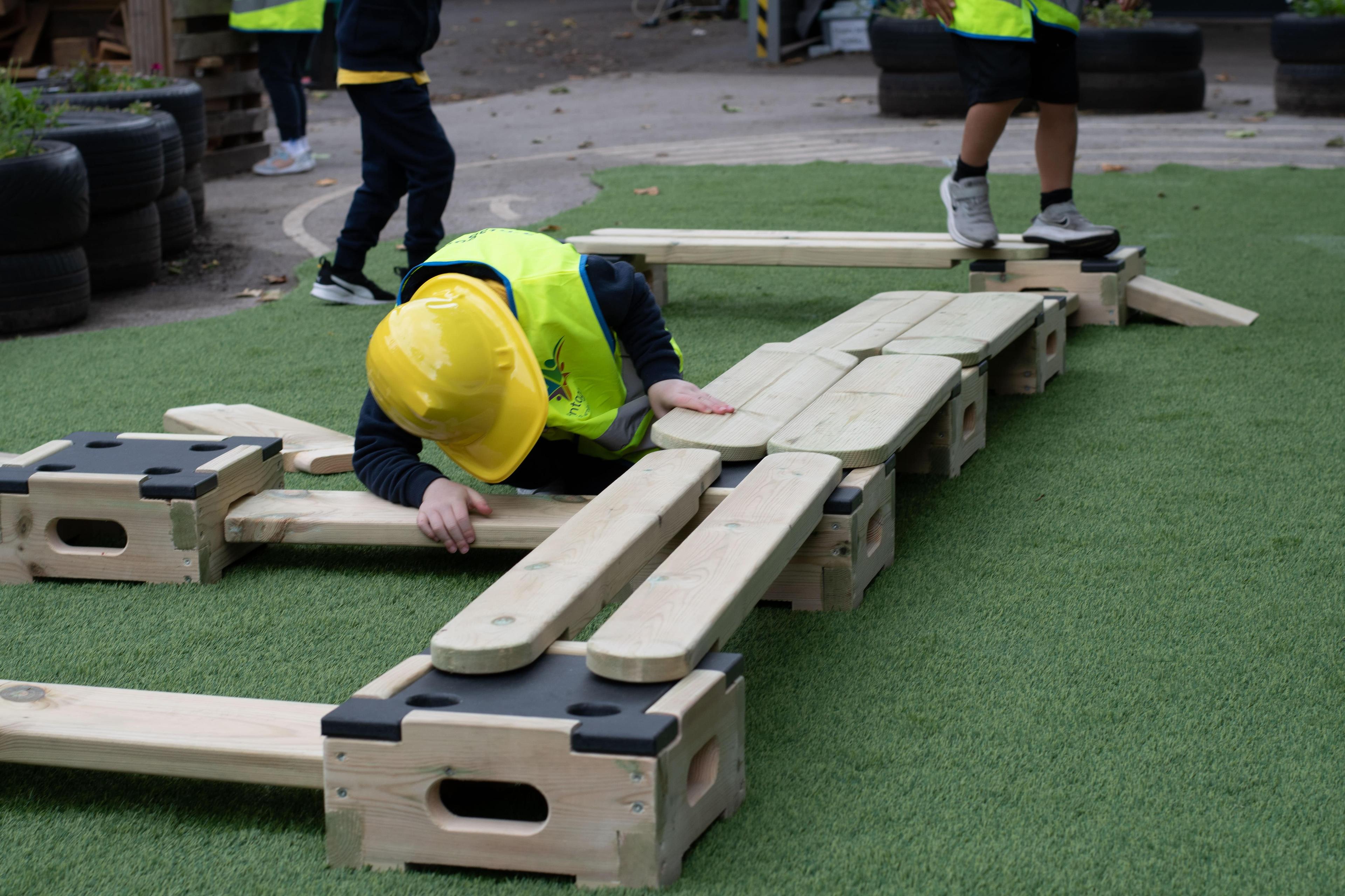 A child in a yellow builder's hat connecting together some play builder planks that are part of the Sports Premium Fundamental Balance and Coordination Package