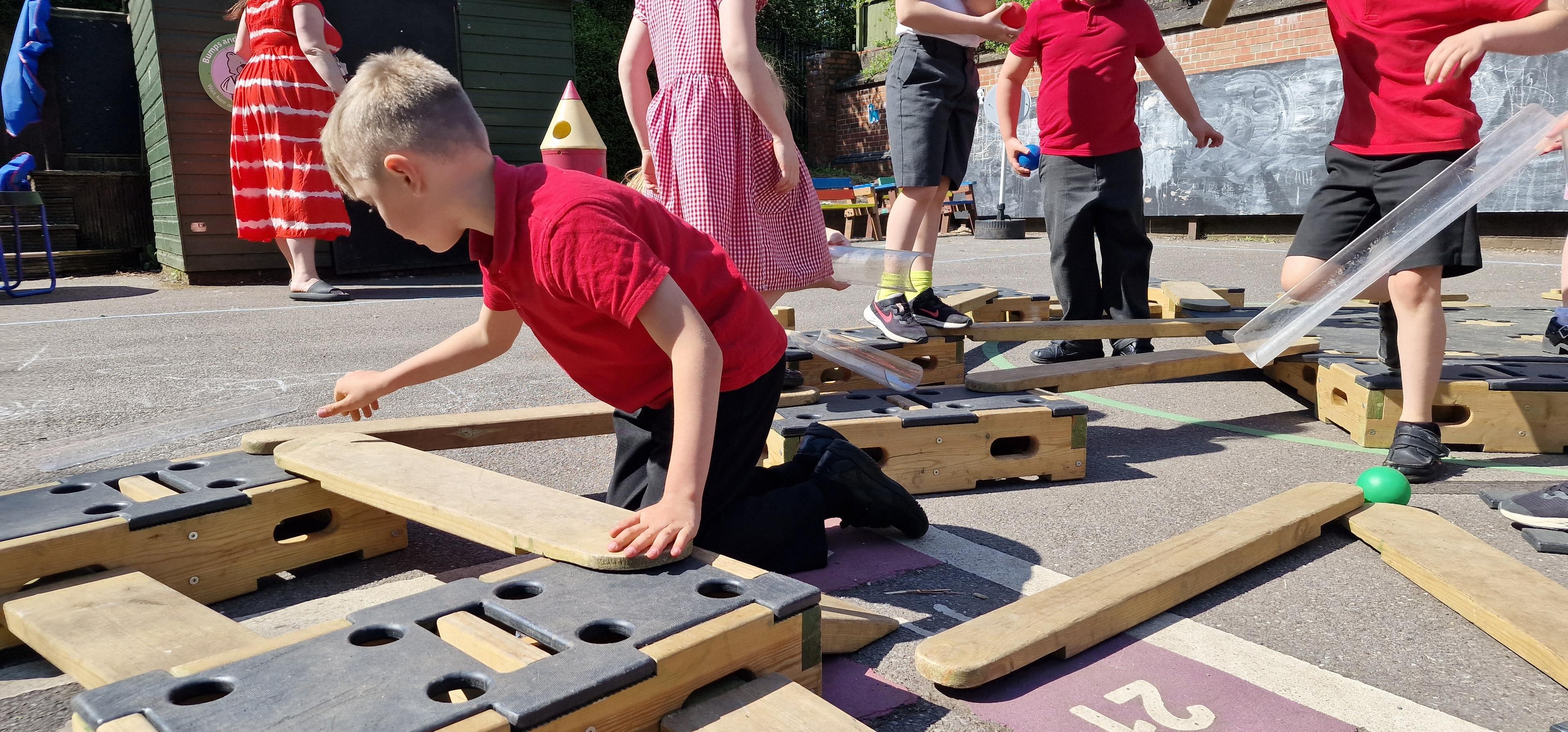 A young child connecting planks to the blocks on the play builder set to create a trail.