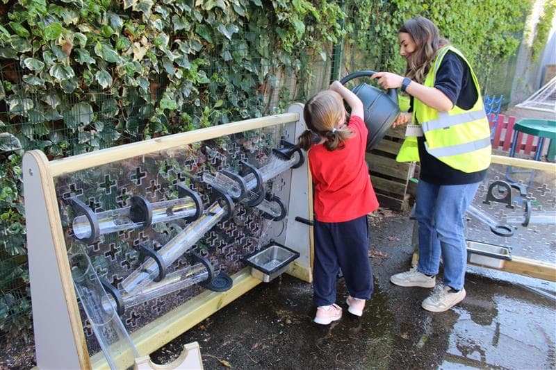 A young girl pouring water down one of the channels on the early years water wall