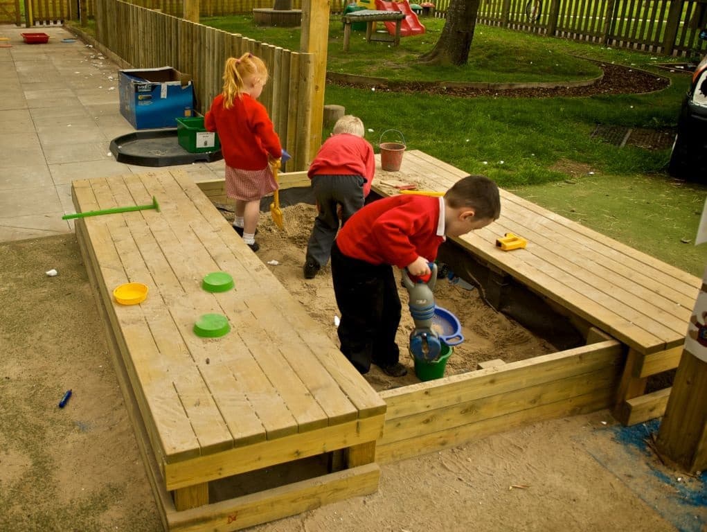 A group of children are digging sand in the large covered sand box with plastic shovels and buckets.
