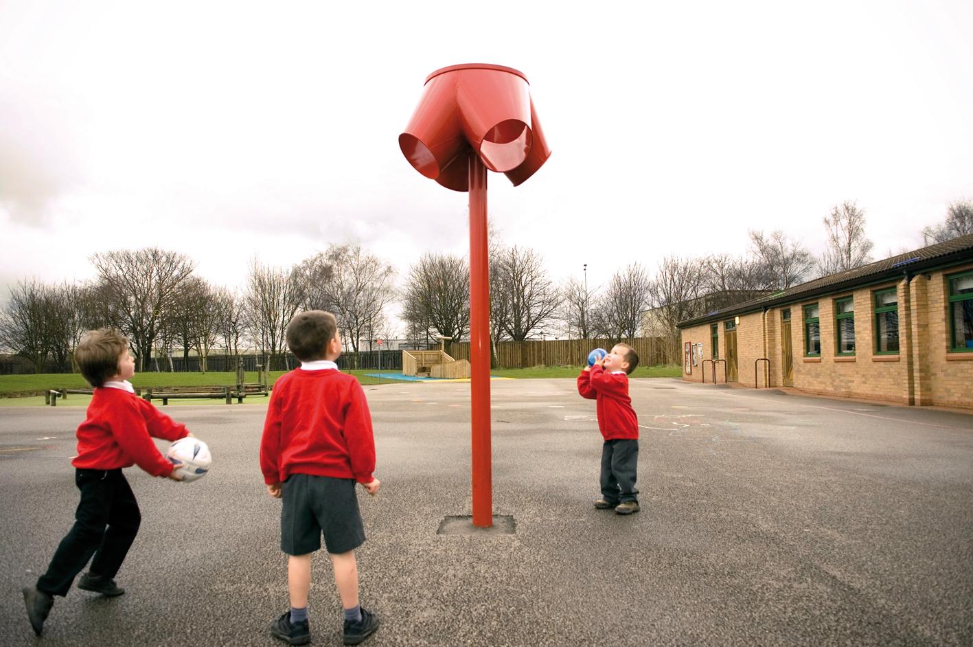 Three children are throwing balls into the 3-way ball shoot on their playground.