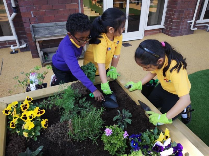 3 children using trowles to plant colourful plants into their quad planter bench
