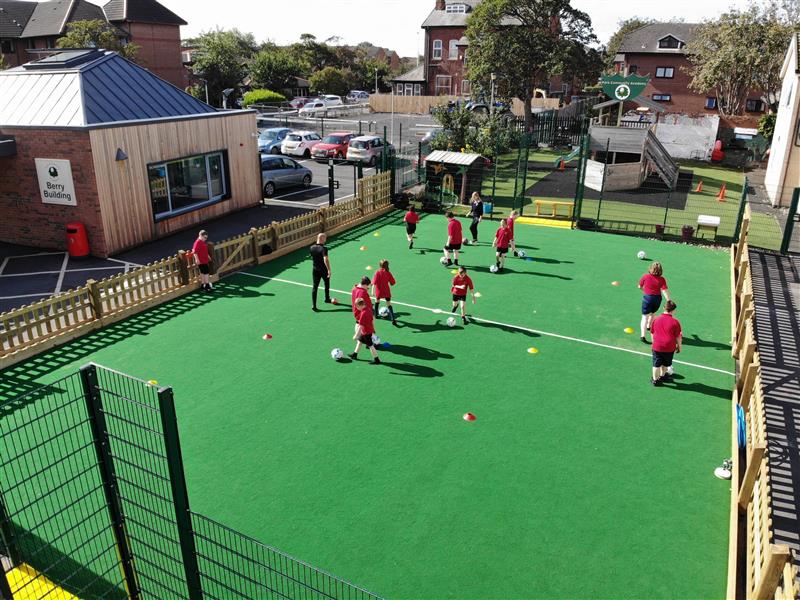 Children playing football games on a multi use games area with a teacher coaching the lesson