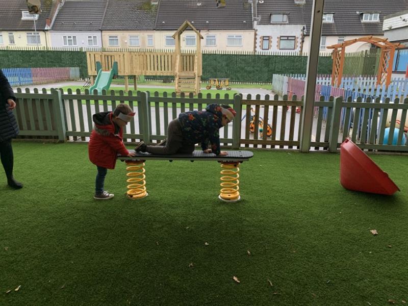 Two children crawling across a spring plank installed onto artificial grass surfacing