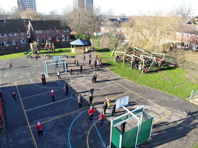 Aerial view of childen playing on playground in a basketball pitch laid out by playground markings whilst more children play on climbing frames. 