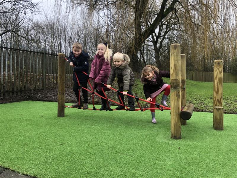 4 children standing on a twist net, balancing and gripping and grasping the red ropes