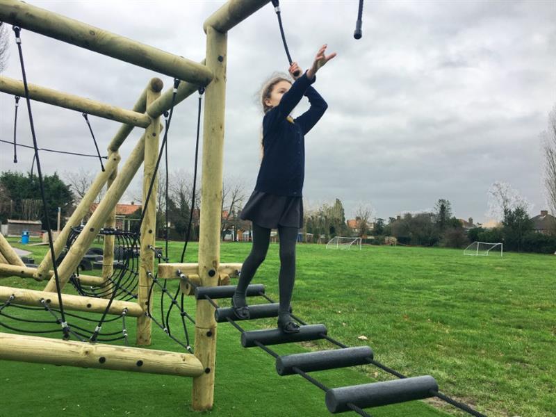 A child tackling the challenges on pentagon plays grizedale forest circuit and reaching for the ropes as they balance carefully across an obstacle