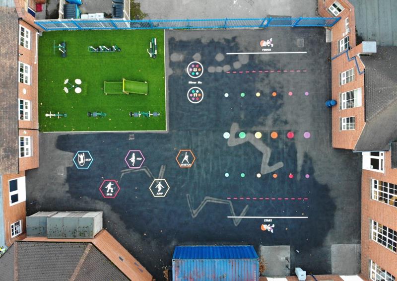 A birds-eye shot of a playground that shows a variety of different playground markings. In the top left corner, an artificial grass surface can be seen. The thermoplastic markings have a variety of different colours.