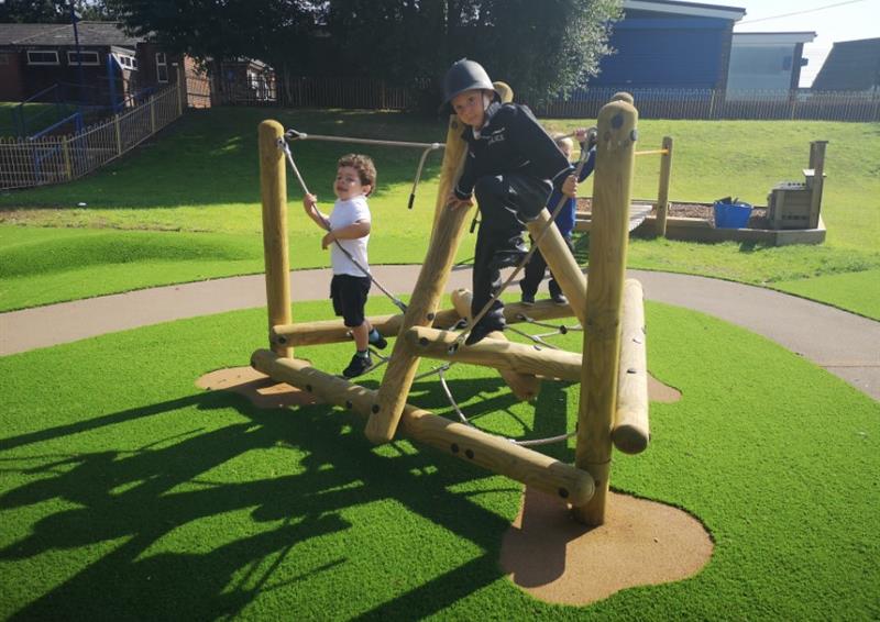 A climbing frame that has been installed on an artificial grass surface. 3 young children are climbing on the equipment.