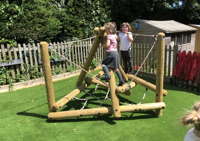A Playframe has been installed on top of artificial grass. A couple of children are playing on the climbing frame, with a wooden fence going around the area.