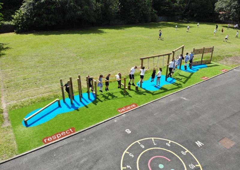 A birds eye view of a class of children playing on their trim trail, artificial grass and positive Saferturf signs are scattered around the edges.