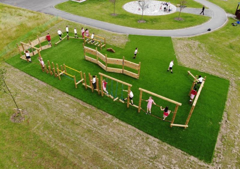 A birds eye view of a class of children playing on their trim trail, artificial grass covers surrounds this area.