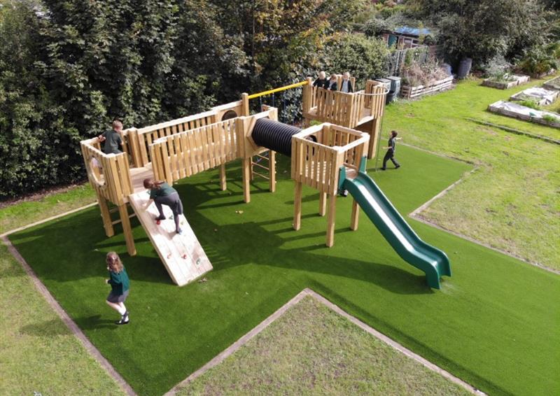 A wooden play tower that has been installed on an artificial grass playground. A group of children are playing on the equipment and engaging with different areas of the play equipment.