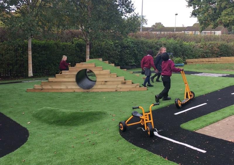 Artificial grass with a Saferturf road marking graphic placed around the area. There is an artificial grass mound in the middle of the area, with an Up and Under block next to it. A group of children are playing in the area.