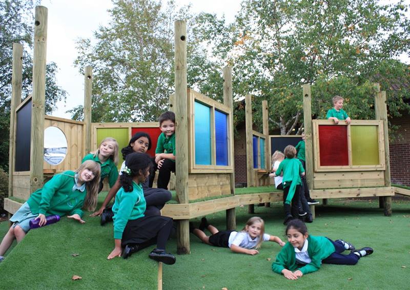 9 children sitting and playing on their new imagination station, 2 children are lying on the artificial grass