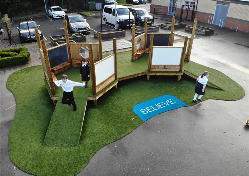 3 children playing on our imagination station, 2 are on the equipment and 1 is walking on the artificial grass.