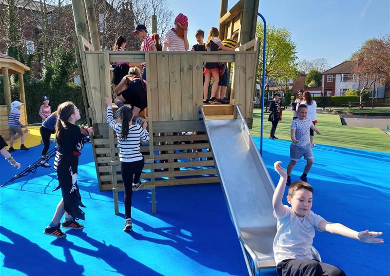 15 children playing on our north sea galleon, one boy is sliding down the slide and the rest of the children are playing on or around the galleon.