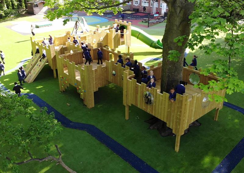 A class of children playing on top of the bespoke treehouse, teachers are standing around accompanying them.