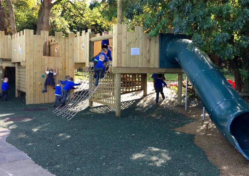 11 children playing on the bespoke treehouse, 3 children are climbing up the ropes on the side of the treehouse.