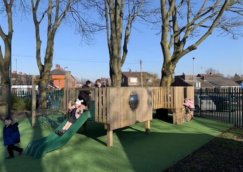 5 children playing on their bespoke treehouse, 1 young girl is sliding down the slide and another young girl is climbing up the climbing wall on the side of the treehouse.
